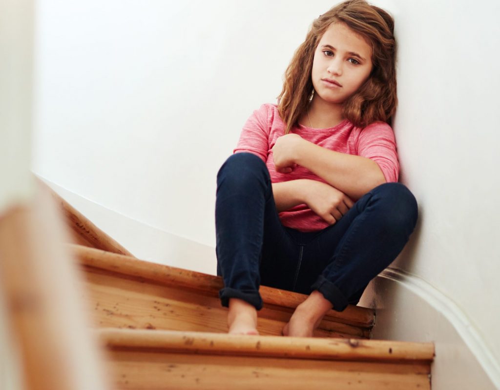 Shot of a little girl looking sad while sitting on the stairs at home